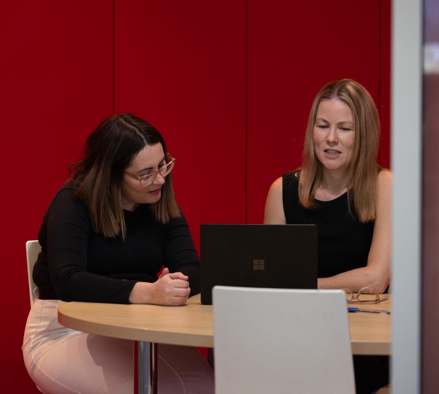 2 ladies seated at an office table going over data on a laptop